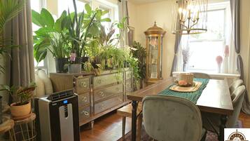A dining area with a wooden table, chairs, and a variety of potted plants.