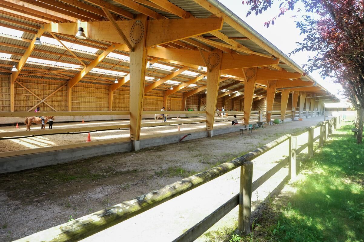 A covered equestrian arena with a dirt track, wooden beams, and a fenced perimeter.