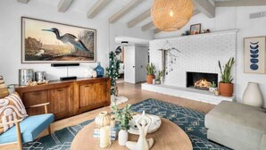 Uma sala de estar espaçosa com lareira de tijolos brancos, um quadro grande de um pássaro e teto de madeira.