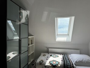 Un dormitorio con tragaluz, una cama con ropa de cama estampada, un radiador blanco y un armario con puerta de cristal.