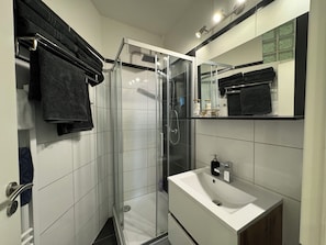 Un baño moderno con ducha de vidrio, un lavabo blanco y un espejo sobre él.