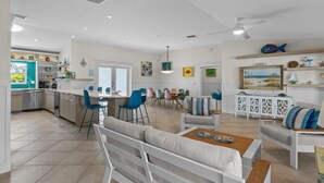A spacious living area with a dining table, chairs, and a sofa. There is a kitchen area with a dishwasher and a window.