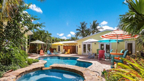 A pool area with multiple pools and lounge chairs, surrounded by tropical plants and a sunny sky.