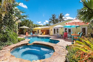 A pool area with multiple pools and lounge chairs, surrounded by tropical plants and a sunny sky.