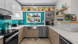 A modern kitchen with a teal backsplash, stainless steel appliances, and a view of the outside through a window.
