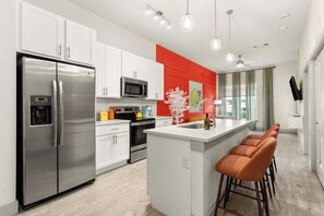 Una cocina moderna con gabinetes blancos, electrodomésticos de acero inoxidable, una pared de acento roja y una zona de bar con taburetes.