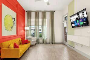 Una sala moderna con un sofá amarillo, un sillón blanco y un televisor de pantalla plana grande montado en la pared, mostrando varios servicios de transmisión.