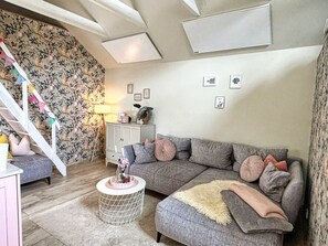 A cozy living room with a grey sectional sofa, a small round side table, and a staircase with floral wallpaper.
