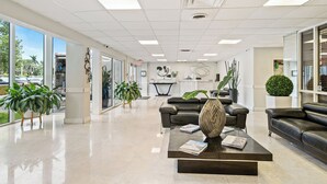 Eine großzügige Lobby mit einer Rezeption, einer Sitzecke und großen Fenstern mit Blick ins Freie.