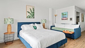 Ein Hotelzimmer mit einem großen Bett, einem kleineren Bett und einem Sofa. Zwei Wandlampen und ein Bild eines Lieferwagens sind an der Wand angebracht.