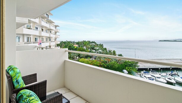 Ein Balkon mit Korbmöbeln, Blick auf das Meer und eine Marina mit Booten.