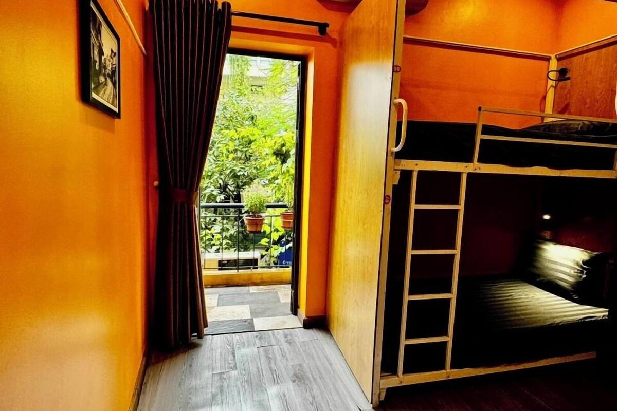 A room with orange walls, a bunk bed, a wooden floor, a window with curtains, and a framed picture on the wall.
