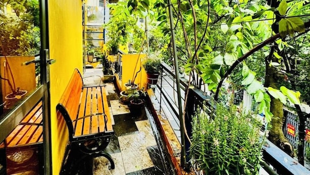 A narrow outdoor balcony with a yellow awning, a wooden bench, a small table, and potted plants. - Autumn Hanoi House Bat Su (Hanoi)