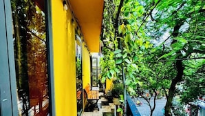 A corridor with a checkered floor, yellow walls, and a view of a street with trees and a parked car. - Autumn Hanoi House Bat Su (Hanoi)