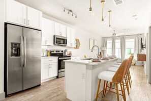 Uma cozinha moderna com armários brancos, eletrodomésticos de aço inoxidável, uma ilha central com banquetas e iluminação pendente.