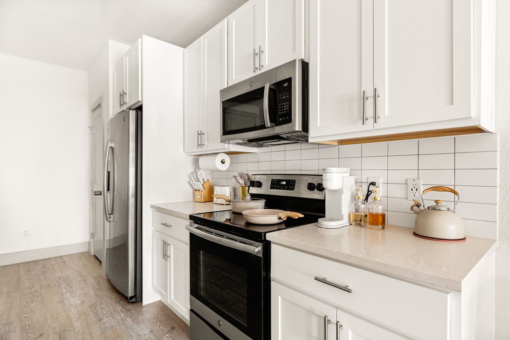 A modern kitchen with white cabinets, stainless steel appliances, and a wooden countertop.