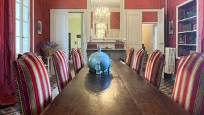 Une salle à manger avec une longue table, des chaises à rayures, un lustre et une bibliothèque.