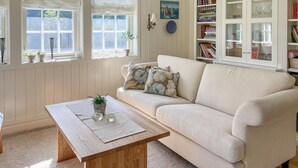 En hyggelig stue med en beige sofa, et træbord og en reol fyldt med bøger og pynteting.