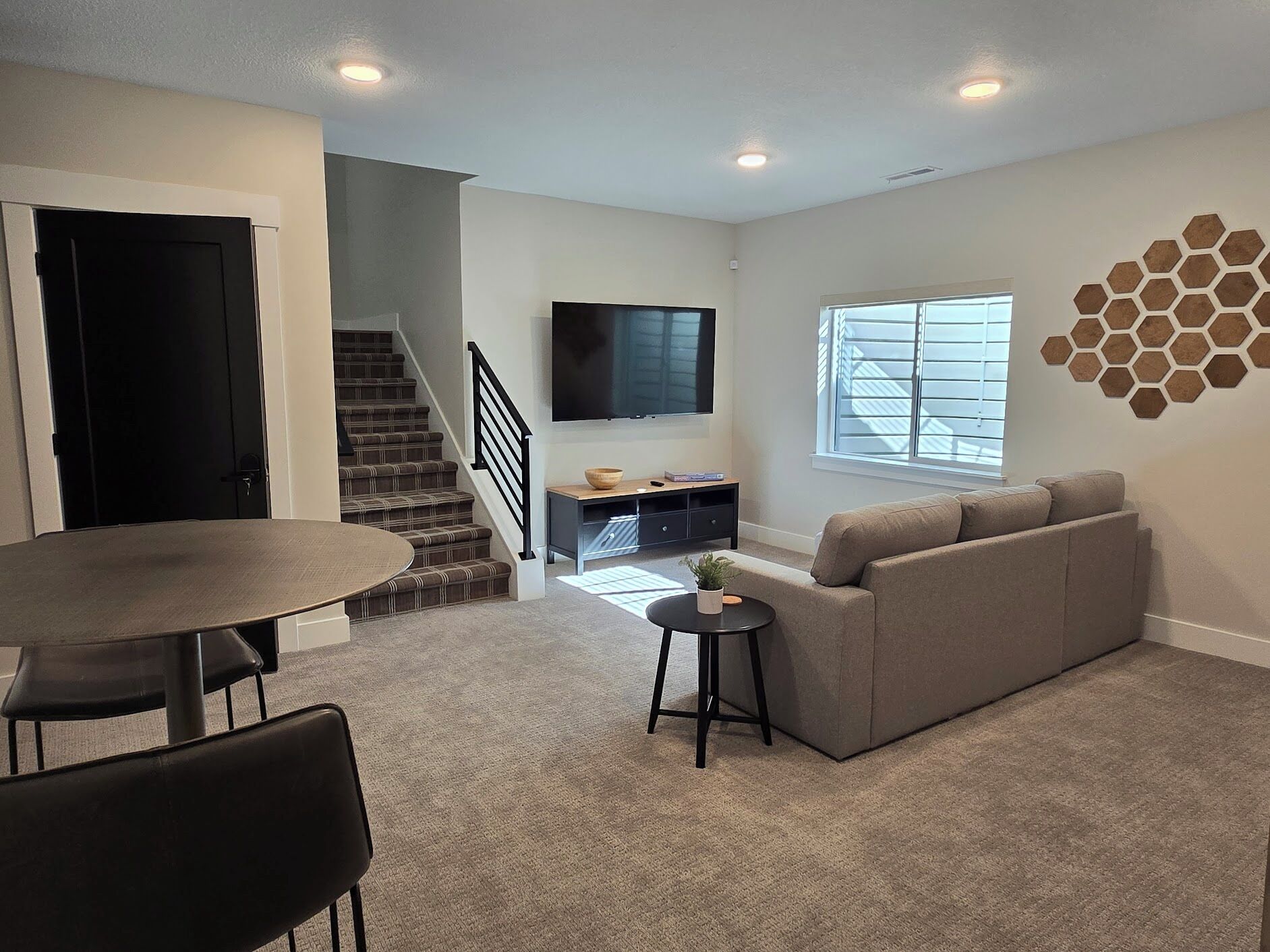Una sala de estar moderna con una escalera, un televisor de pantalla plana, un sofá y una zona de comedor.