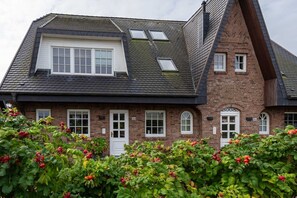 Uma casa de dois andares com telhado inclinado, janelas em sacadas e fachada de tijolos.