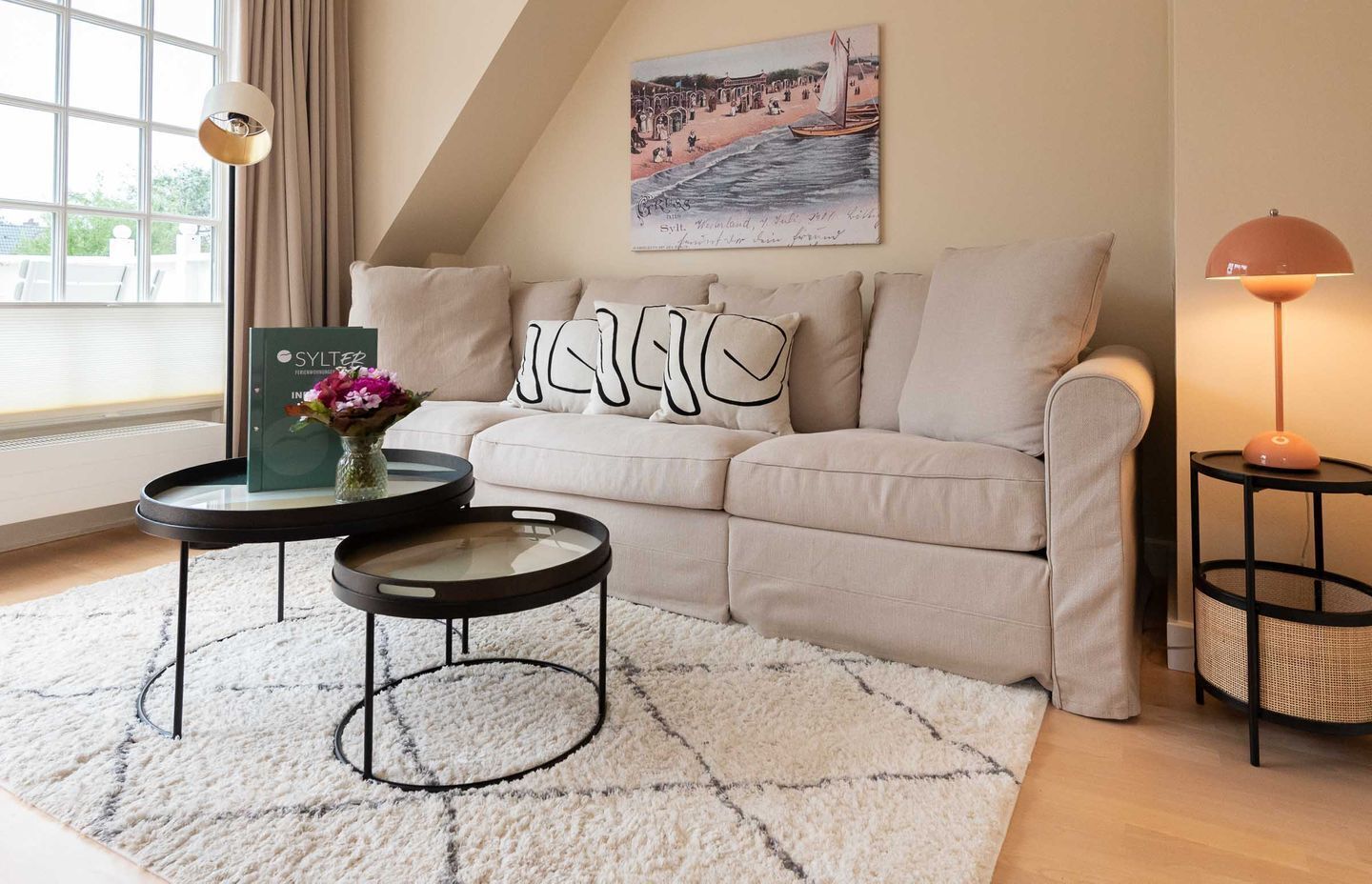 Ein gemütliches Wohnzimmer mit einer Couch, zwei Beistelltischen, einer dekorativen Vase und einem Bild an der Wand.