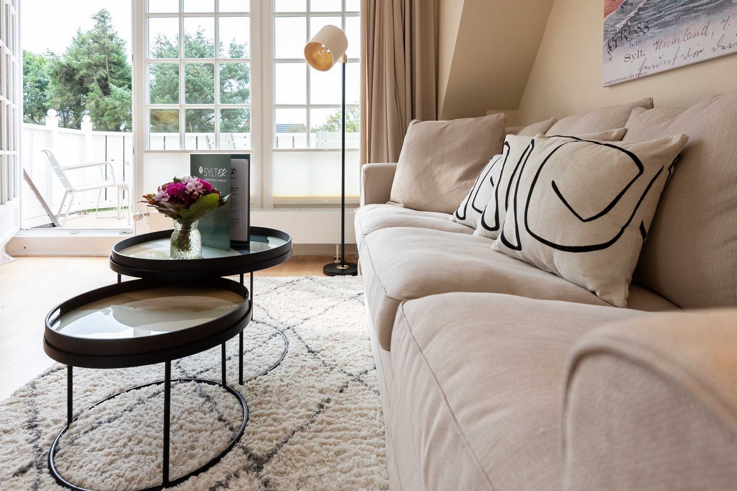 A living room with a beige sofa, a round coffee table with a vase of flowers, and a floor lamp.