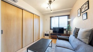 A modern living room with a sofa, a coffee table, a TV, and a sliding door closet. - UNIFY 203 (Sapporo)