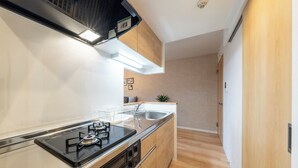 A modern kitchen with a gas stove, stainless steel appliances, wooden cabinets, and a light-colored backsplash. - UNIFY 203 (Sapporo)