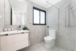 A modern bathroom with a glass shower enclosure, a white toilet, and a vanity with a mirror and storage containers.