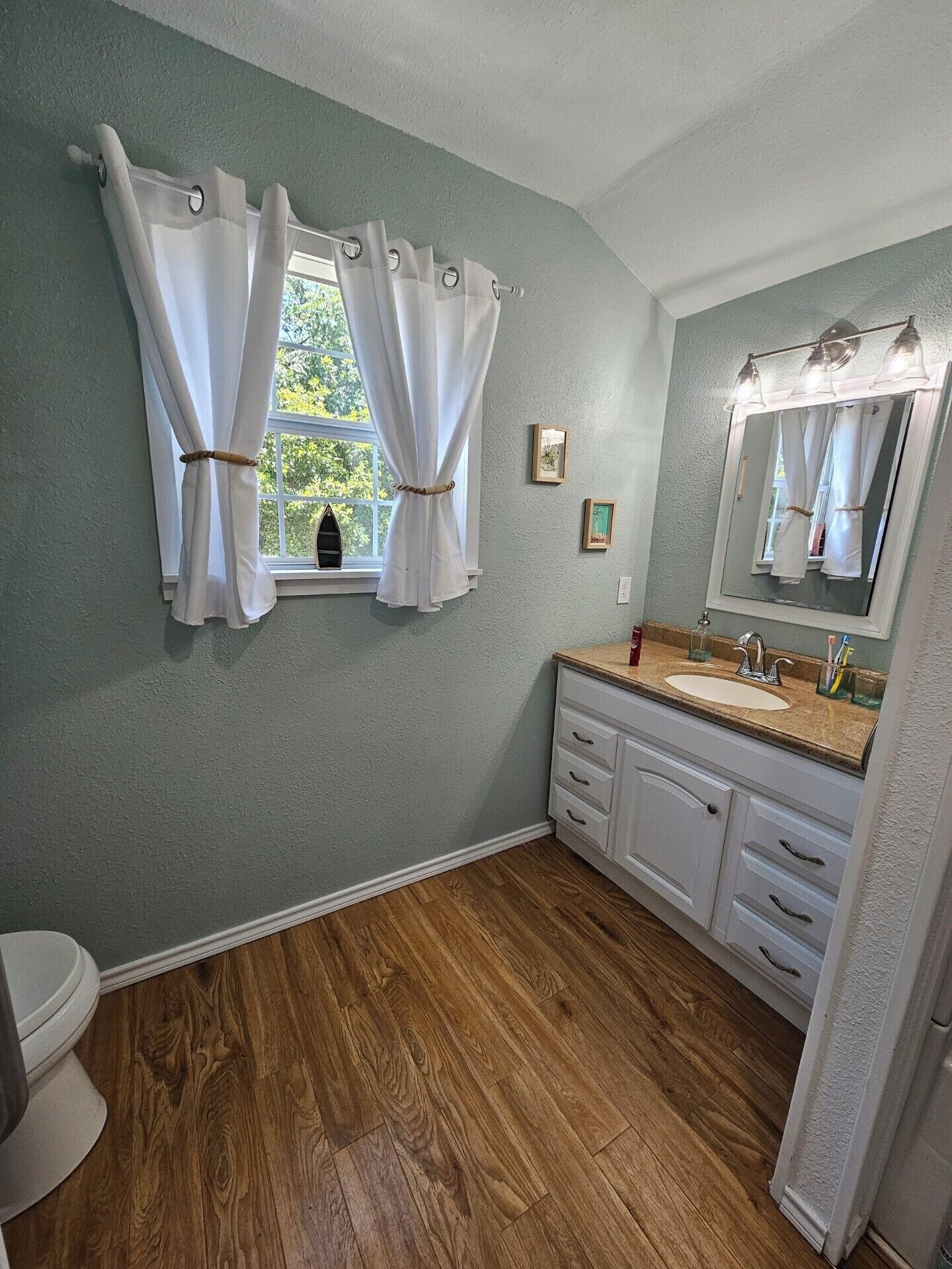 Une salle de bain avec une fenêtre, un lavabo, un miroir et un plancher en bois.