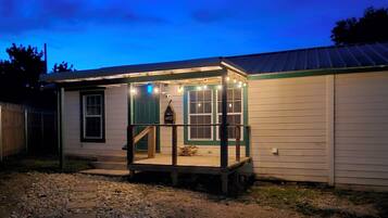 Simple, single-story building with a porch and flat roof, featuring a series of windows and a gravel pathway.