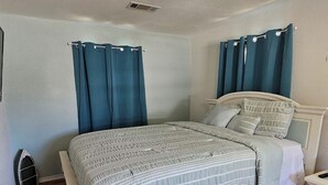 Een slaapkamer met een bed, gordijnen, een nachtkastje en een klein kastje.