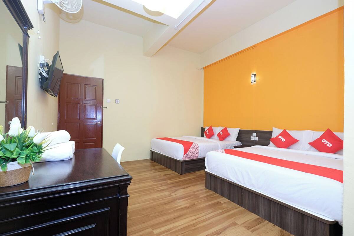 Habitación de hotel con dos camas, un escritorio de madera, un espejo, un ventilador y una ventana con vista al cielo.