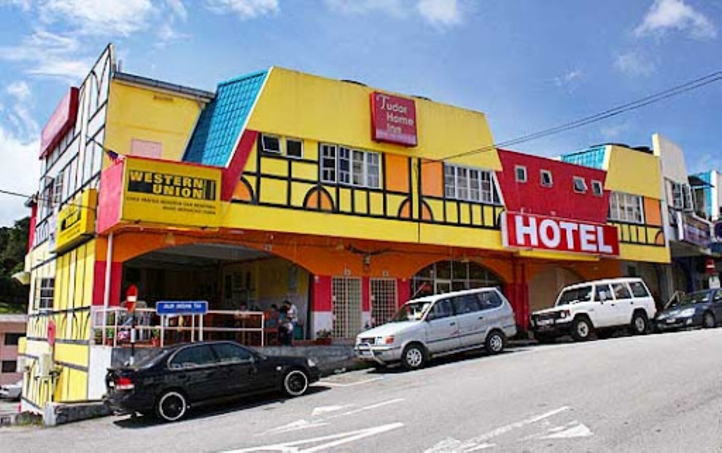 Ett hotell med en gul fasad, en röd skylt som visar att det är ett Tudor Home Inn, och en Western Union-servicepunkt.