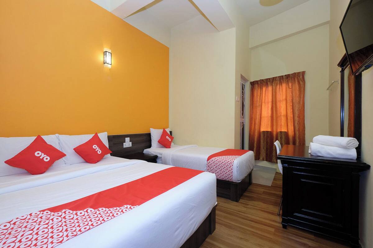 Habitación de hotel con dos camas, cada una con ropa de cama roja y blanca, una mesita de noche, un escritorio y una silla.