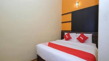 A hotel room with a bed, two pillows, a red and white bedspread, and a wall with a light fixture.