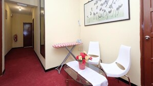 A hallway with a red carpet, a white chair, a bench, a table with a red and white checkered tablecloth, and a framed artwork on the wall. - Hotel Tudor Cameron Highland (Brinchang)