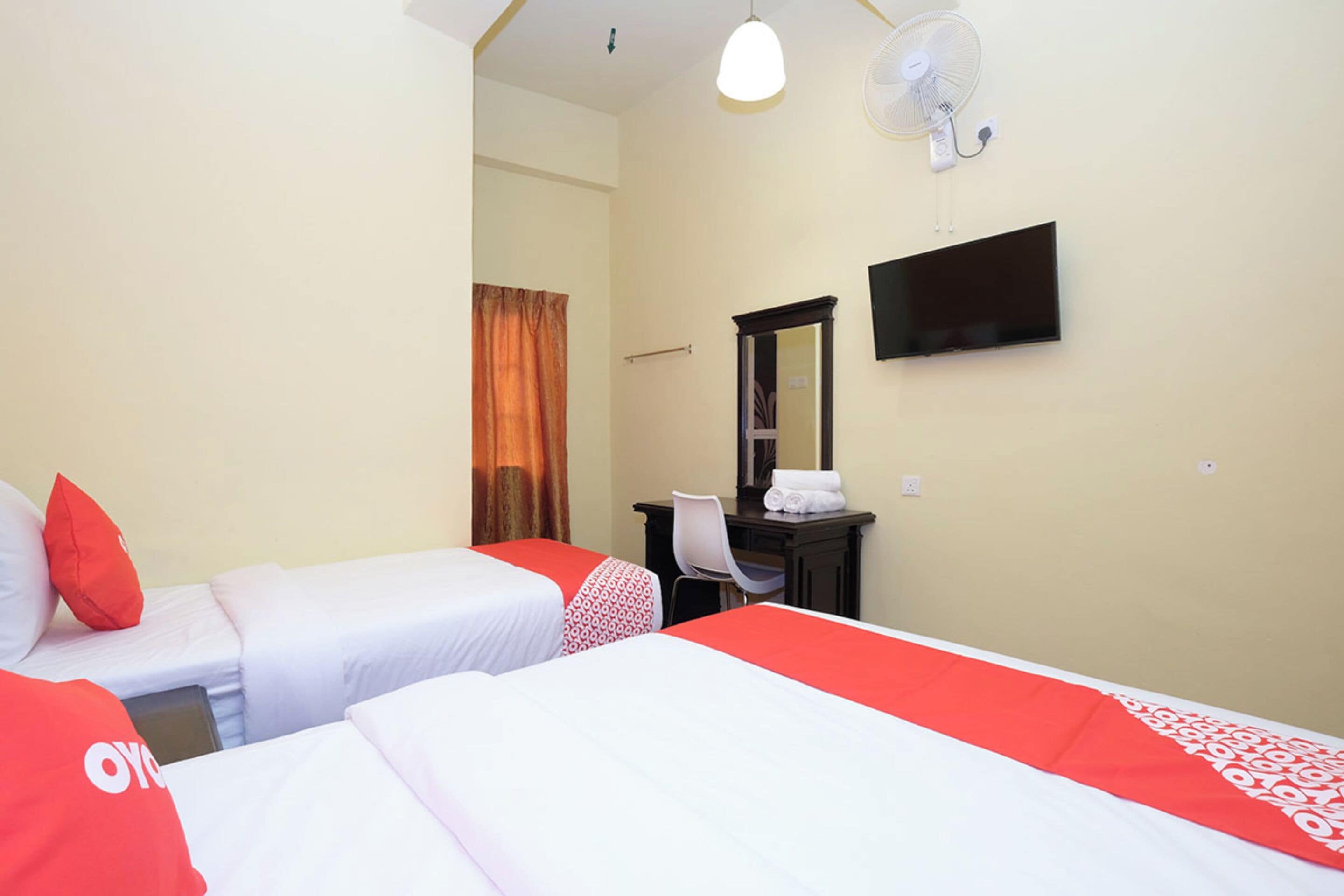 Une chambre d’hôtel avec deux lits, un bureau, une chaise, une télévision et un ventilateur.
