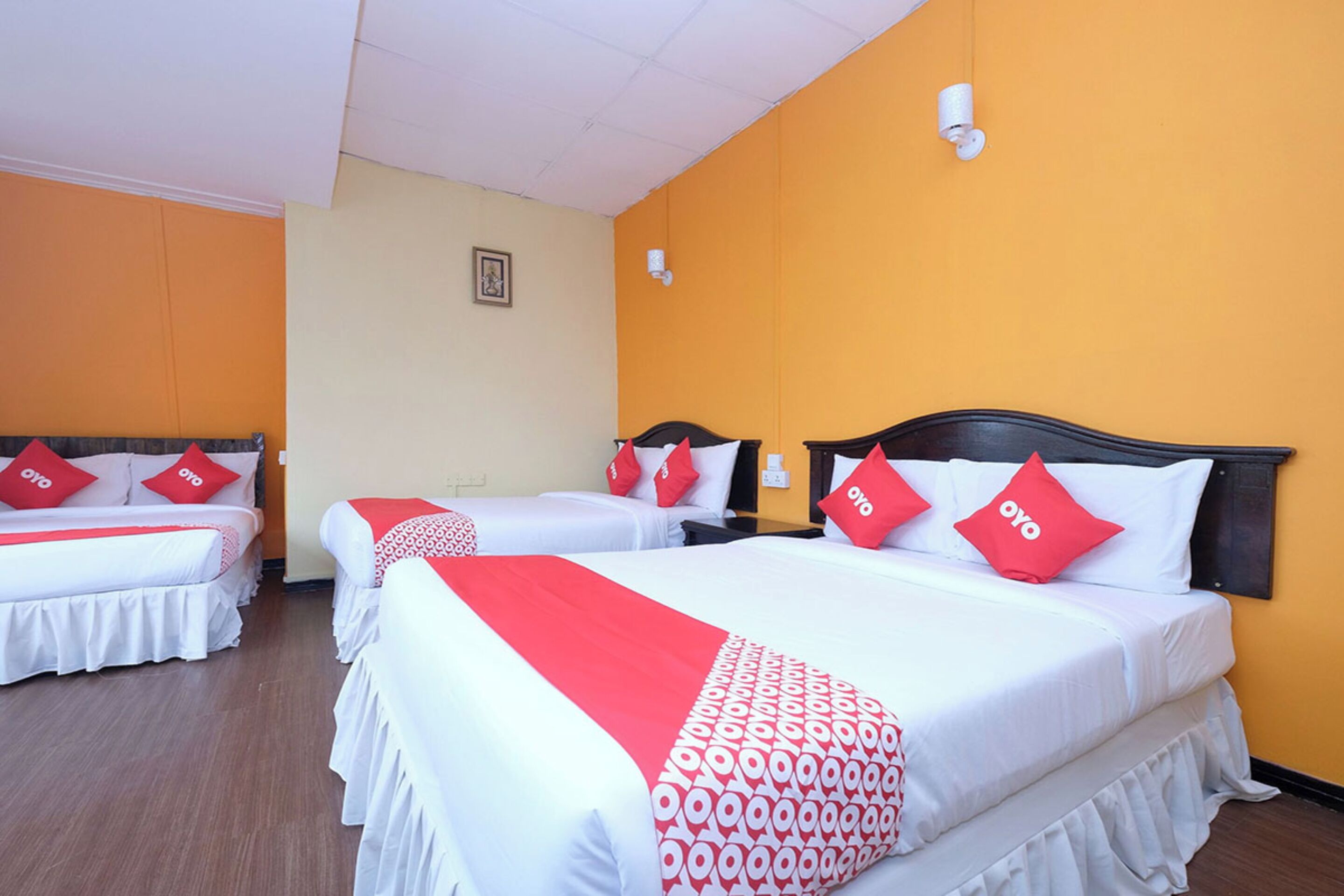 Habitación de hotel con tres camas, cada una con ropa blanca y detalles en rojo, y una pared de color amarillo.