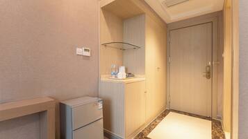 Una camera d'albergo compatta con angolo cottura, un piccolo frigorifero, uno scaffale in vetro con articoli da toilette e un accesso al bagno.