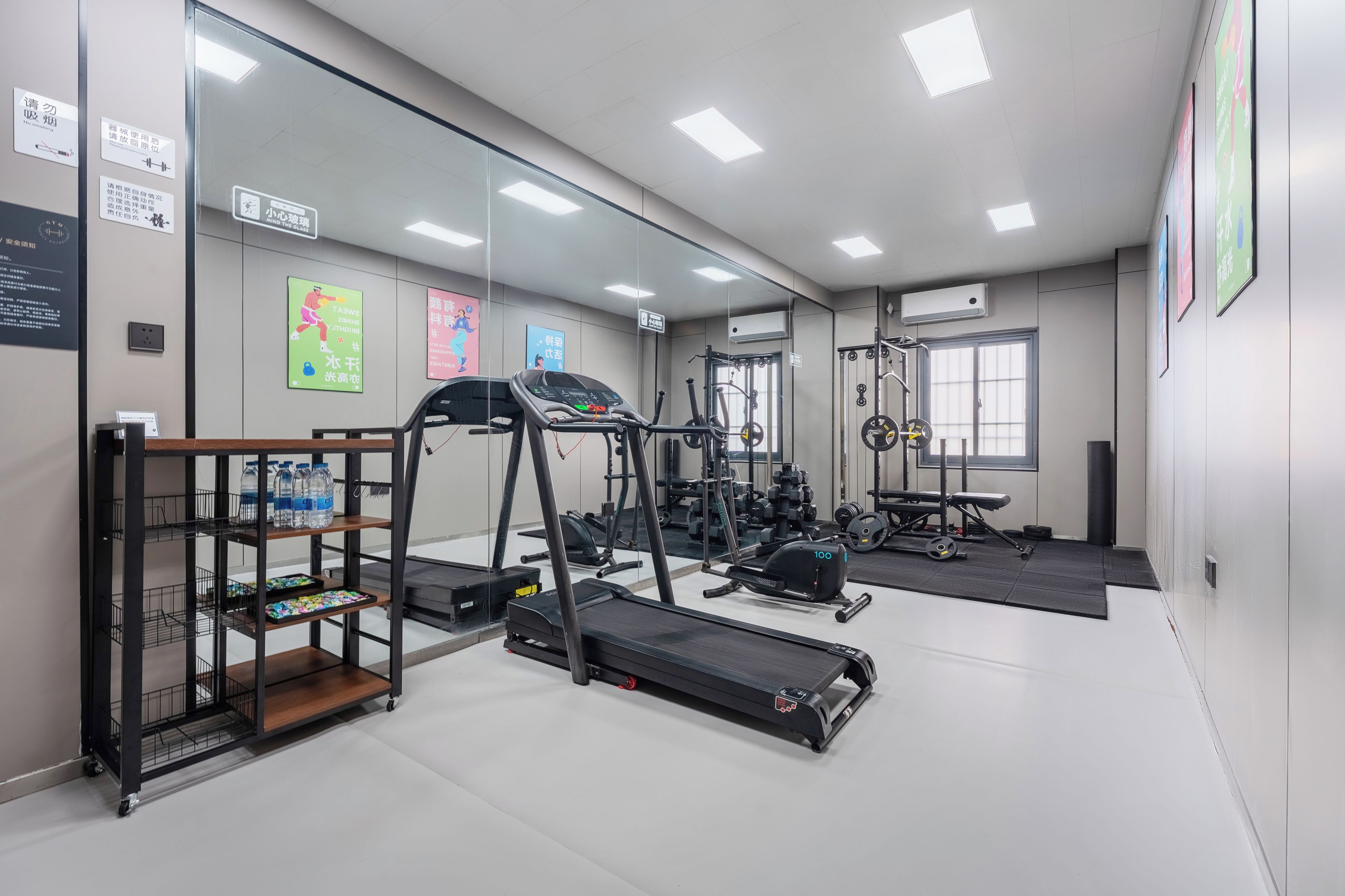 Ein Fitnessstudio mit Laufband, Kraftgeräten und einem Wagen für Wasserflaschen.