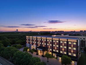 Hotel com vários andares, entrada coberta e vista para o horizonte da cidade ao entardecer.