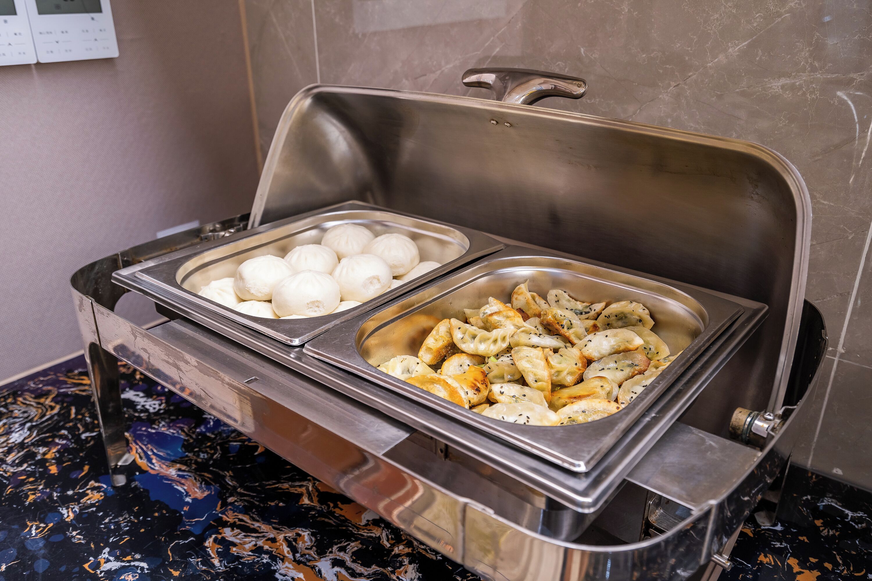 A buffet with two stainless steel chafing dishes, one containing dumplings and the other containing boiled eggs.