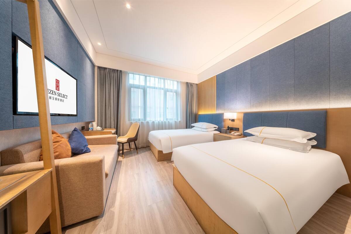 A hotel room with a bed, two bedside tables, a desk, a chair, and a TV screen displaying 'EZEN SELECT'.