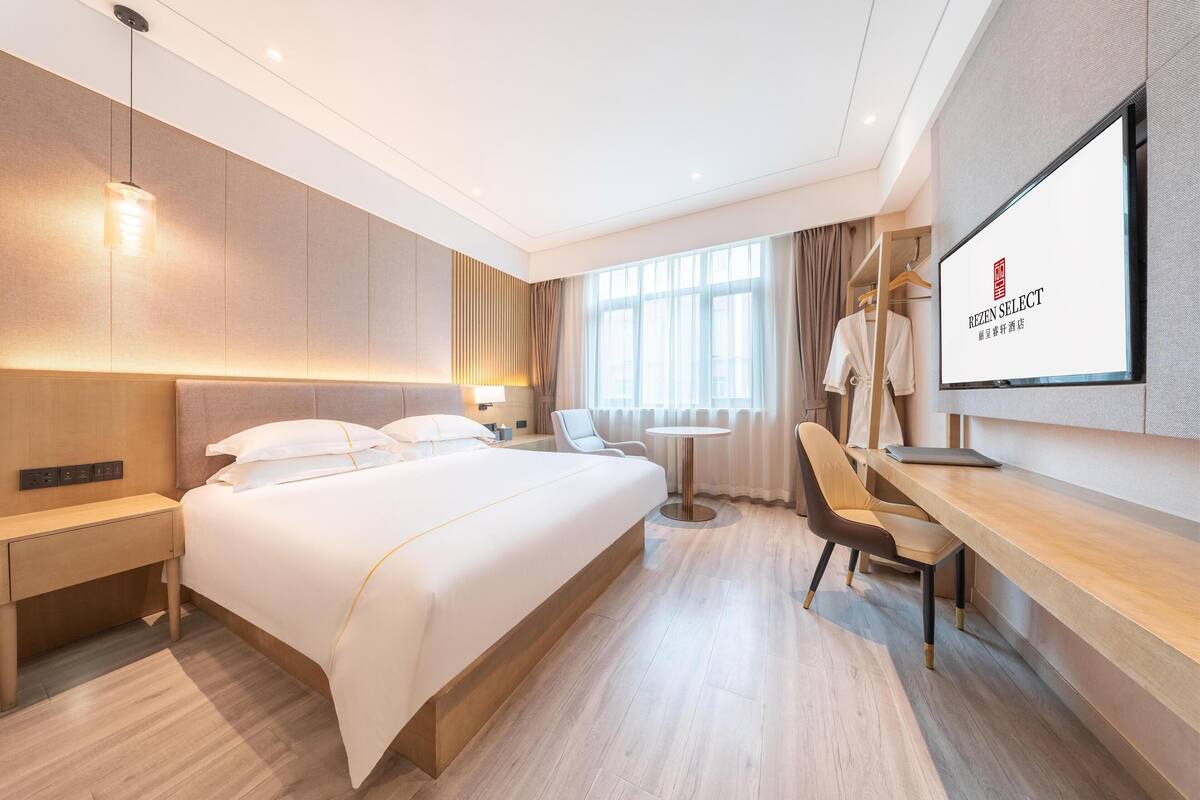 A modern hotel room with a large bed, bedside tables, a desk, and a TV.