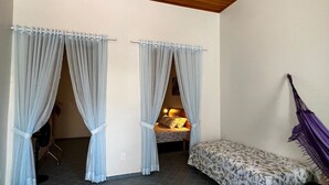 A room with two curtained windows, a bed with a floral bedspread, and a purple hammock.