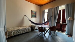 A room with a hammock, a bed, a small table with chairs, and a painting on the wall.