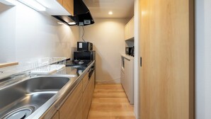 A compact kitchen with a stainless steel sink, wooden cabinets, a microwave, and a stove. - UNISON (Sapporo)