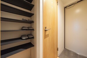 Een gang met een houten deur, een zwart metalen schoenenrek en een gesloten deur aan het einde.