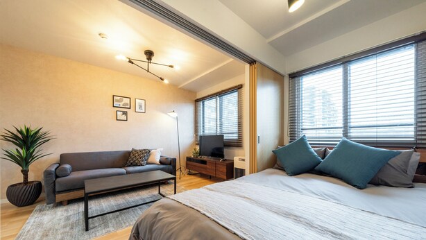 A modern bedroom with a large bed, a sofa, a TV, and a plant. - UNISON (Sapporo)